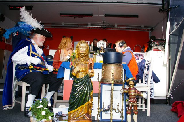 Peter Schmorl von der Stader Fastnachtsgilde (li.) mit den Moderatoren Ilka Petersen und Holger Ponik. Im Vordergrund Stade-Accessoires wie die Heilige Gertrud und Peter Männcken