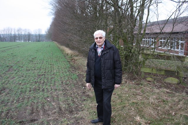 Ortsbürgermeister Kurt Hölzer steht am Acker, auf dem der Kunstrasenplatz gebaut werden soll. Rechts die Grundschule, im Hintergrund die Ostfriesische Tee Gesellschaft (OTG) in Meilsen