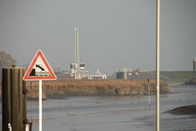 Blick vom ehemaligen Anleger zum Süderelbe-Sperrwerk. Schemenhaft sind die Aufbauten der Elbfähre zu erkennen