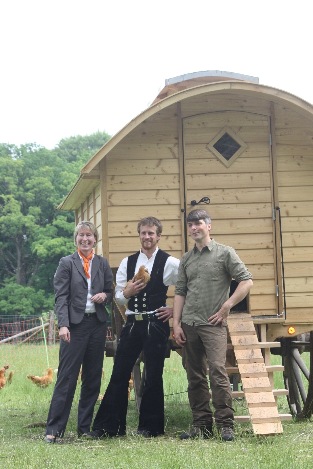 Ute Stolberg (Volksbank Lüneburger Heide) freut sich mit Benjamin Leinecker (Mitte) und Johannes Buhr (beide VNP-Stiftung Naturschutzpark) über den neuen Hühnerwagen auf dem Schulbauernhof in Wilsede
