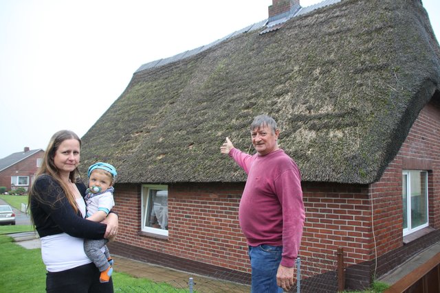 Gustav von Reith zeigt auf das beschädigte Reetdach. Nicole Ikemeyer  - mit Enkelsohn Michel - fühlt sich der Dohlenplage machtlos ausgesetzt