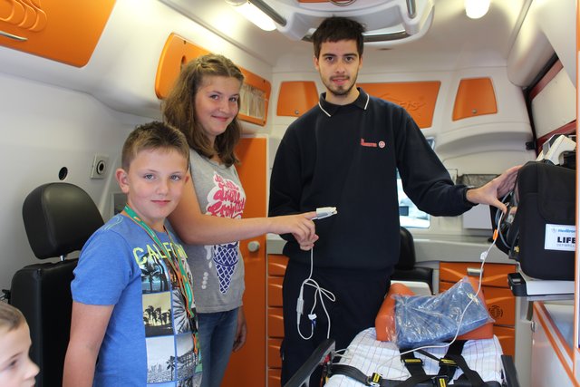 Christopher Hirch zeigt Anna-Lena und Marvin im Rettungswagen der Johanniter, wie das Blutdruckmessgerät funktioniert