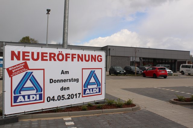Ein großes Schild auf dem Parkplatz weist auf die Neueröffnung des dahinter zu sehenden ALDI-Marktes hin