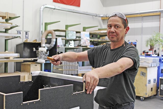 Andreas Kastning befestigt mit gezielten Hammerschlägen Aluminiumschienen an Boden und Deckel der Kisten, so passen sie später genau aufeinander