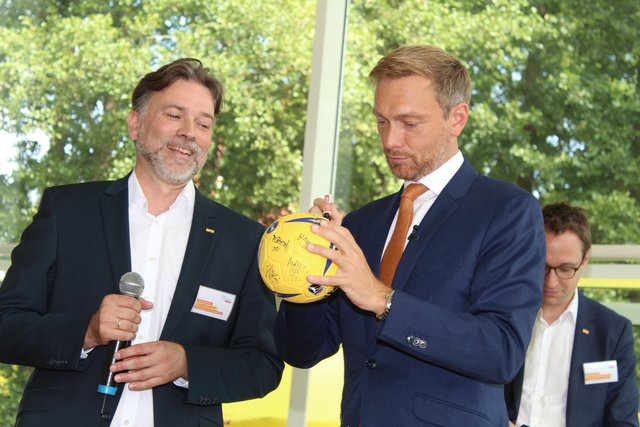Christian Lindner (re.) signiert einen Handball, auf dem sich schon die BSV-Bundesligaspielerinnen verewigt haben
