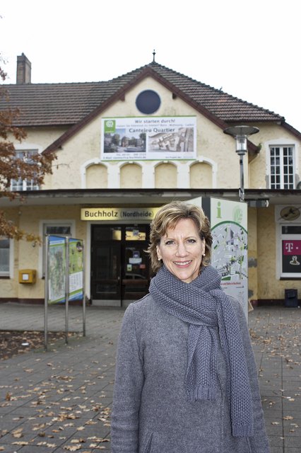 Tari Van Noy (terra Real Estate) vor dem Buchholzer Bahnhof, an dem das große Plakat angebracht wurde