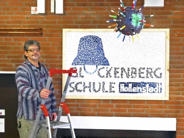 Hausmeister Peter Eckhoff vor dem neuen Schild der Glockenbergschule