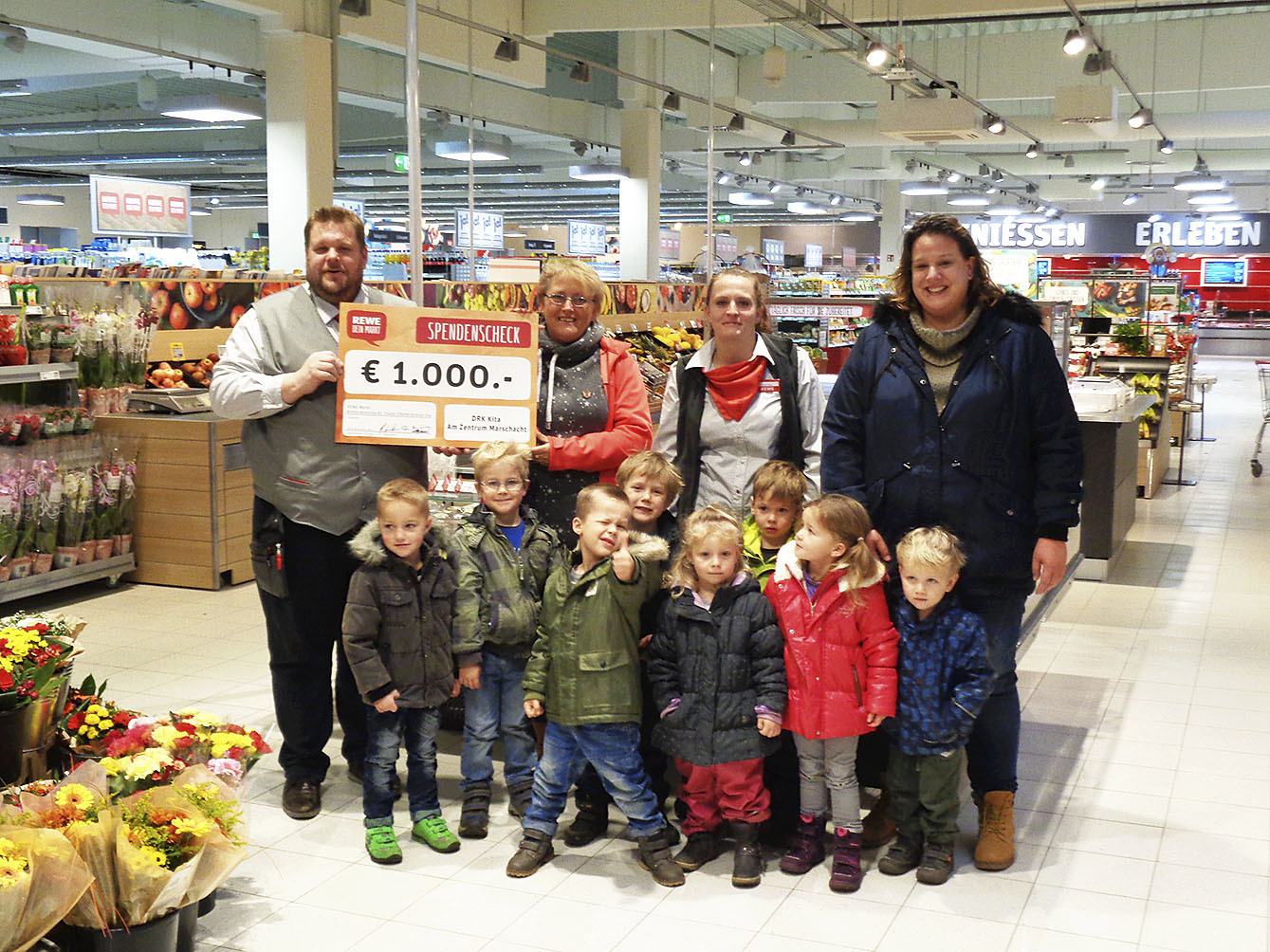 REWE-Marktmanager Andreas Westphal und Mitarbeiterin Alexandra Thiele (2.v.re.) übergeben den symbolischen Scheck an Kita-Leiterin Heidi Röhsler (2.v.li.), Erzieherin Mona-Alexandra Michelsen (re.) und die Kinder der DRK-Kindertagesstätte.