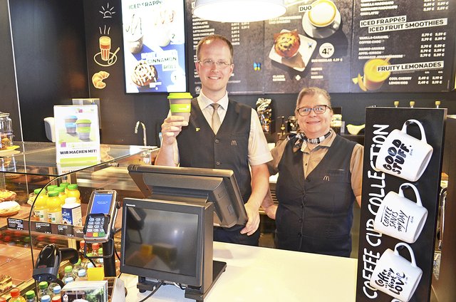 Bezirksleiter Carsten Tiedt und Restaurant-Managerin Stefanie Kofler weisen auf den Tauschbecher und die Café-Spezialitäten hin