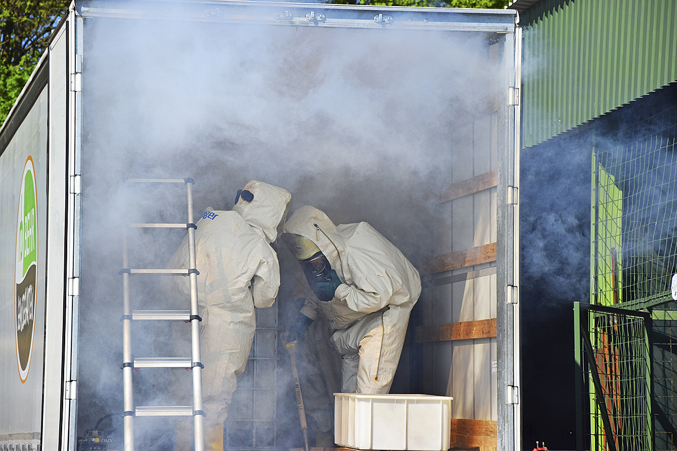 Realistische Übung bei starkem Rauch: Feuerwehrleute in Chemikalienschutzanzügen beseitigen die Gefahrenstoffe aus einem Lkw