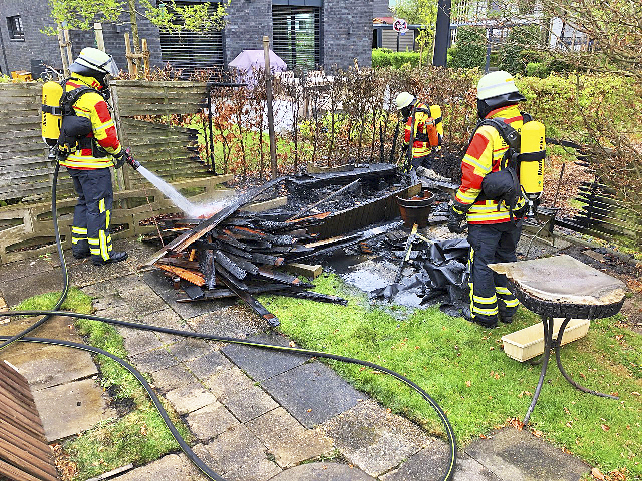 Hittfelder Feuerwehrleute löschen das in Brand geratene Holz in einem Garten in Emmelndorf