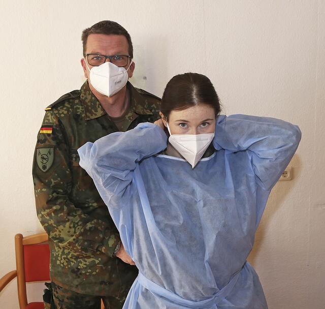 Der Hauptfeldwebel hilft der Oberstabsgefreiten, die blaue Schutzkleidung anzulegen