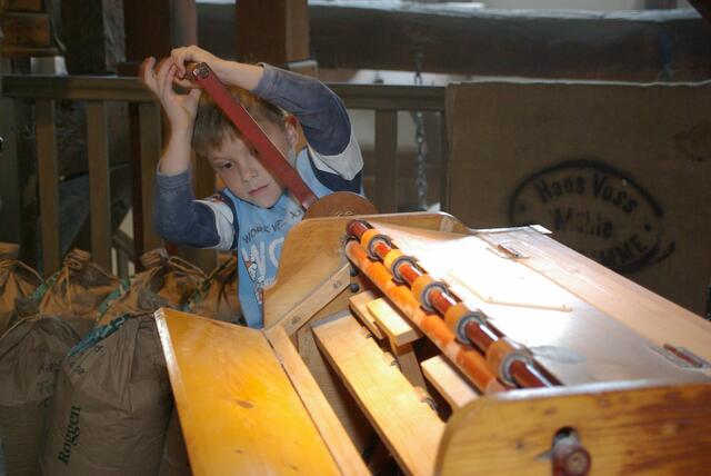 Ein Junge probiert eine Sackreinigungsmaschine aus, Mühlenmuseum Moisburg - Bild FLMK, Die Mehlsäcke aus Jute wurden vor dem Wiederbefüllen durch die Sackreinigungsmaschine gedreht und so weitergehend vom Mehl befreit | Foto: FLMK
