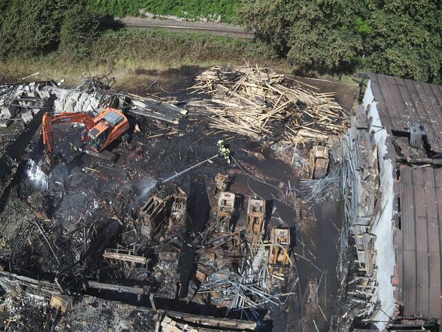 Drohnenaufnahme von der ausgebrannten Lagerhalle. Ein Bagger zieht die Glutnester auseinander  | Foto: FFW Harsefeld