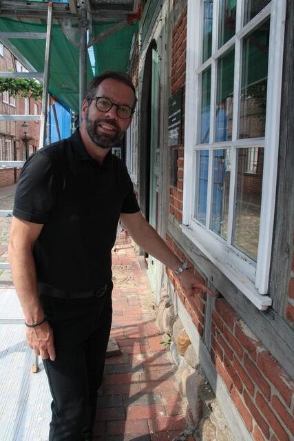 Architekt Christoph Frenzel zeigt die Ziegelsteine, die sich langsam aus dem Fachwerk heraus in Richtung Straße neigen