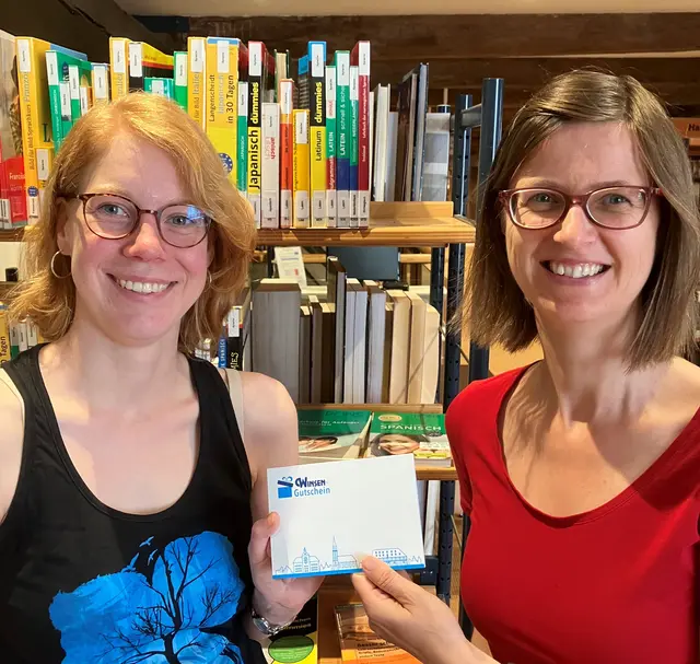 Ines Bader (re.) und Freyja May von der Wirtschaftsförderung der Stadt mit einem der Winsen-Gutscheine, die bei der Aktion „Bücher-Bingo“ von der Stadtbücherei als Preise ausgelobt werden | Foto: Stadt Winsen