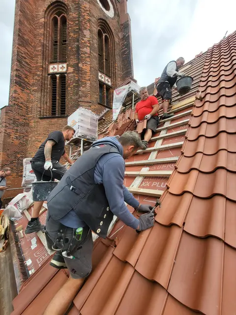 Reges Treiben auf dem Dach - die einen werfen sich Dachziegel zu, die anderen bringen den Mörtel nach oben auf den First. Insgesamt werden 33 Tonnen Material mit Muskelkraft auf dem Dach bewegt