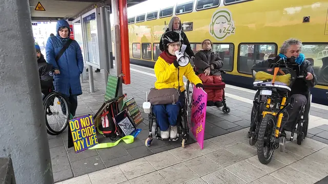 Mit Plakaten und Megaphon protestiert die Gruppe gegen die Barrieren am Bahnhof 