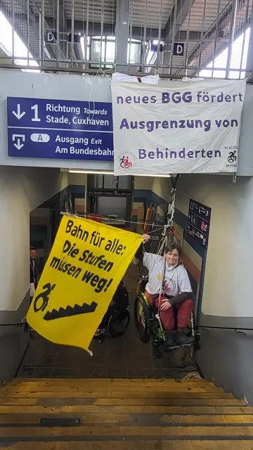 Protest, dass die Reparatur des defekten Aufzug am Bahnhof Buxtehude  ein halbes Jahr lang dauert: Cecile Leconte lässt sich in ihrem Rollstuhl mit einem Seilzug in die Höhe ziehen 