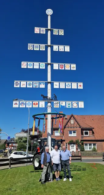 Drei Männer stehen vor einem traditionellen Maibaum