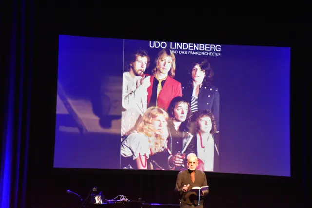 Bertram Engel bei der Lesung vor einem Foto aus den Anfangsjahren von Udo Lindenbergs Panikorchester | Foto: ah