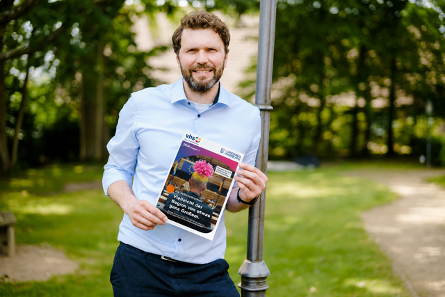 Stefan Baumann präsentiert das neue Programmheft der Kreisvolkshochschule Landkreis Harburg für das Herbst- und Wintersemester 2026.  | Foto: Landkreis Harburg/ (Cover digital bearbeitet)