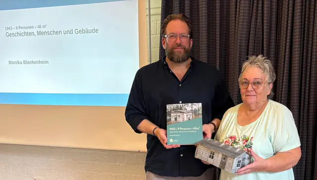 Museumsdirektor Stefan Zimmermann und Autorin Monika Blankenheim zeigen das neue Werk und ein Modell eines Behelfsheims bei der Buchvorstellung am 21.6.2026 im Freilichtmuseum am Kiekeberg. | Foto: FLMK