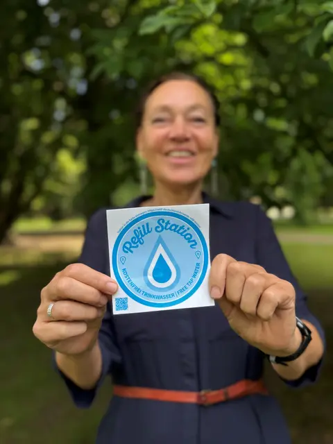 Christiane Vogt, Vorsitzende der Top Trails, zeigt das Refill-Logo, das Wandernde auf dem Heidschnuckenweg an vielen Stationen finden 
