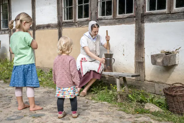 Kinder schauen beim Sommerspaß 21. bis 26. Juli einer Darstellerin der Gelebten Geschichte 1804 beim Buttern zu. | Foto: FLMK