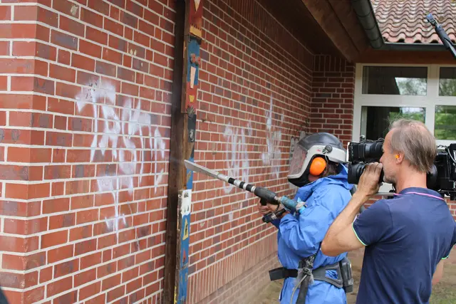 Vor der TV-Kamera im Einsatz: Trono-Mitarbeiter Matthias Johannsen beseitigt im Schutzanzug mit einer Trockeneis-Strahlpistole die Graffiti-Schmierereien an der Hauswand | Foto: ce