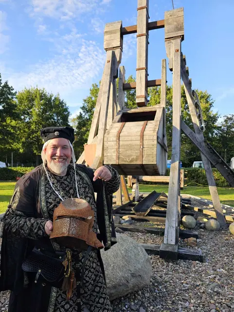 Der Bischof (Udo Onika) präsentiert stolz den eingedellten Helm, der von einer der Steinkugeln der Blide getroffen wurde. Den Helm trug die Isern-Hinnerk-Puppe, die auf der "Burganlage" montiert war. | Foto: Udo Onika